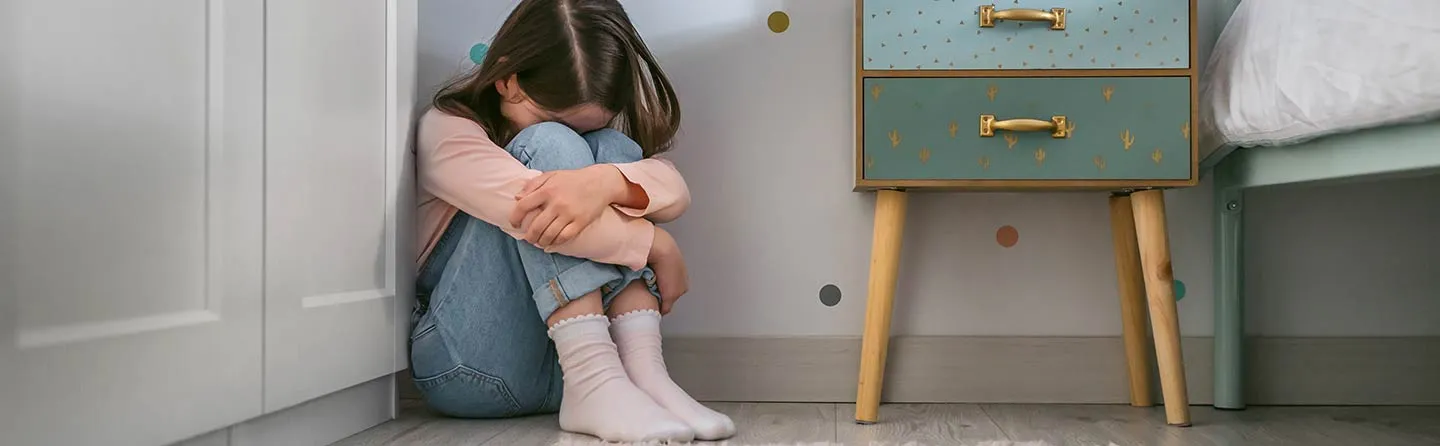 Petite fille assise par terre dans sa chambre, la tête sur les genoux