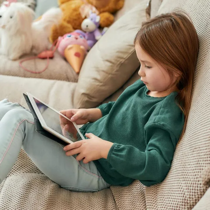 Petite fille assise sur un canapé avec une tablette sur les genous