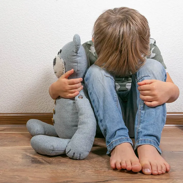 Enfant assis par terre la tête dans les genoux avec un doudou