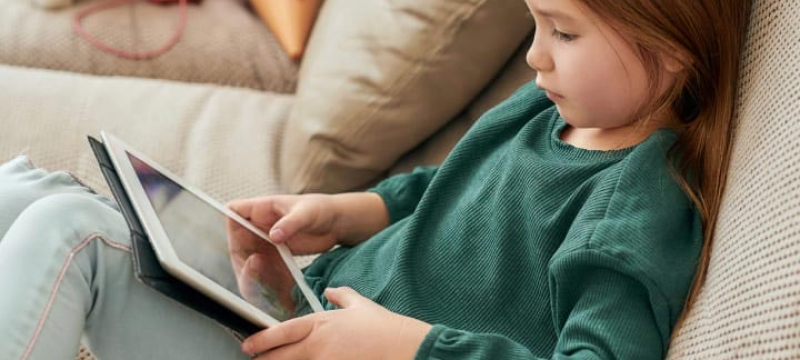 Petite fille assise sur un canapé avec une tablette sur les genous